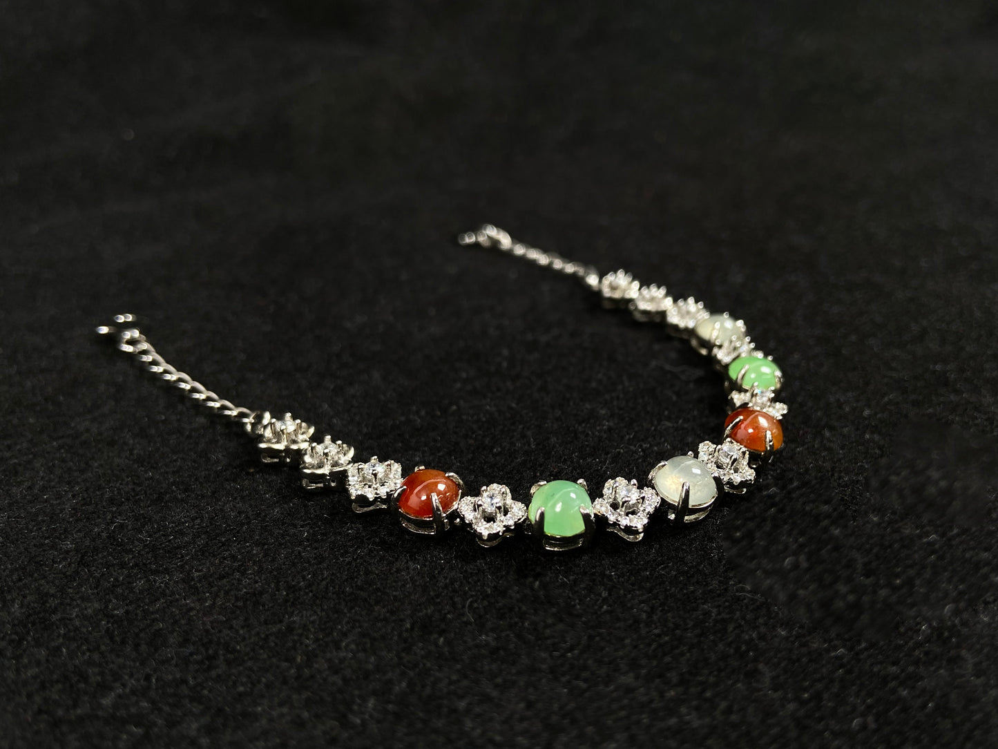 A jadeite bracelet with brown, green, and icy cabochons, each separated by sterling silver flowers set with diamond centers.