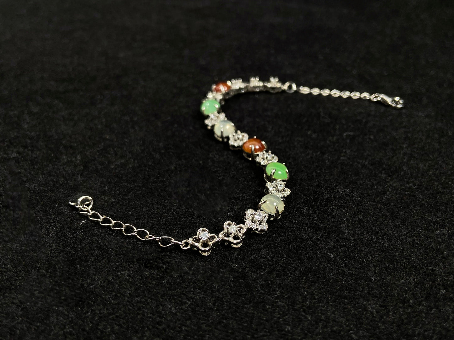 A jadeite bracelet with brown, green, and icy cabochons, each separated by sterling silver flowers set with diamond centers.