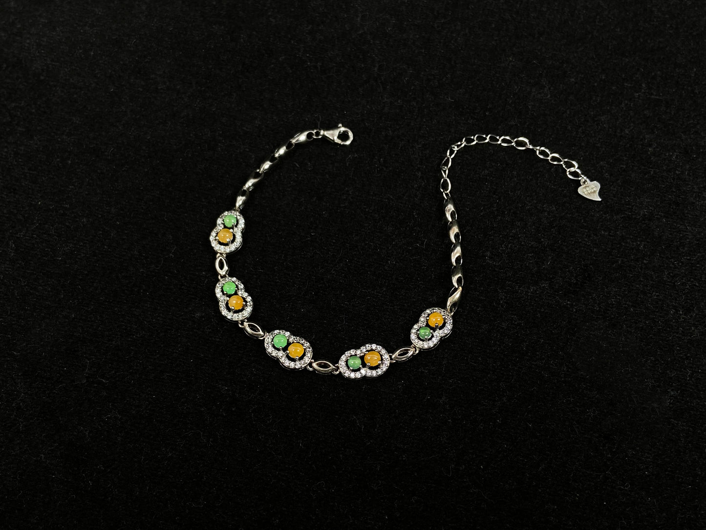 A hollow gourd-shaped bracelet in 925 silver, set with a large yellow cabochon and small apple-green cabochon, accented with diamonds.