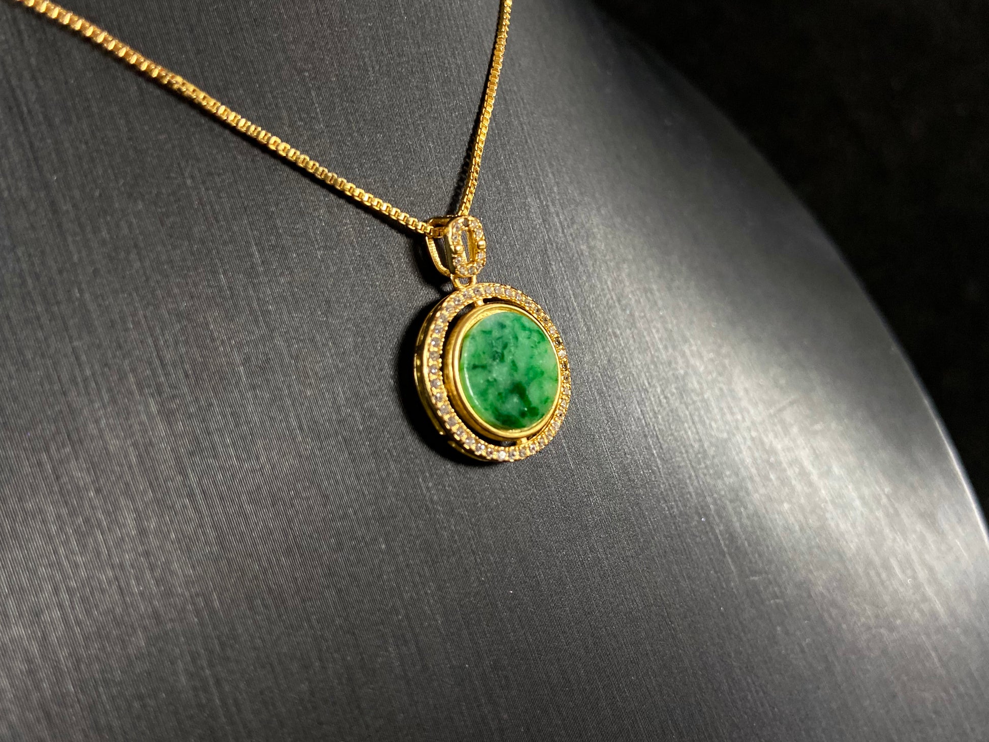 This pendant centers a small, round jadeite with a translucent white base and wisps of green, framed by a wide band of 925 silver.