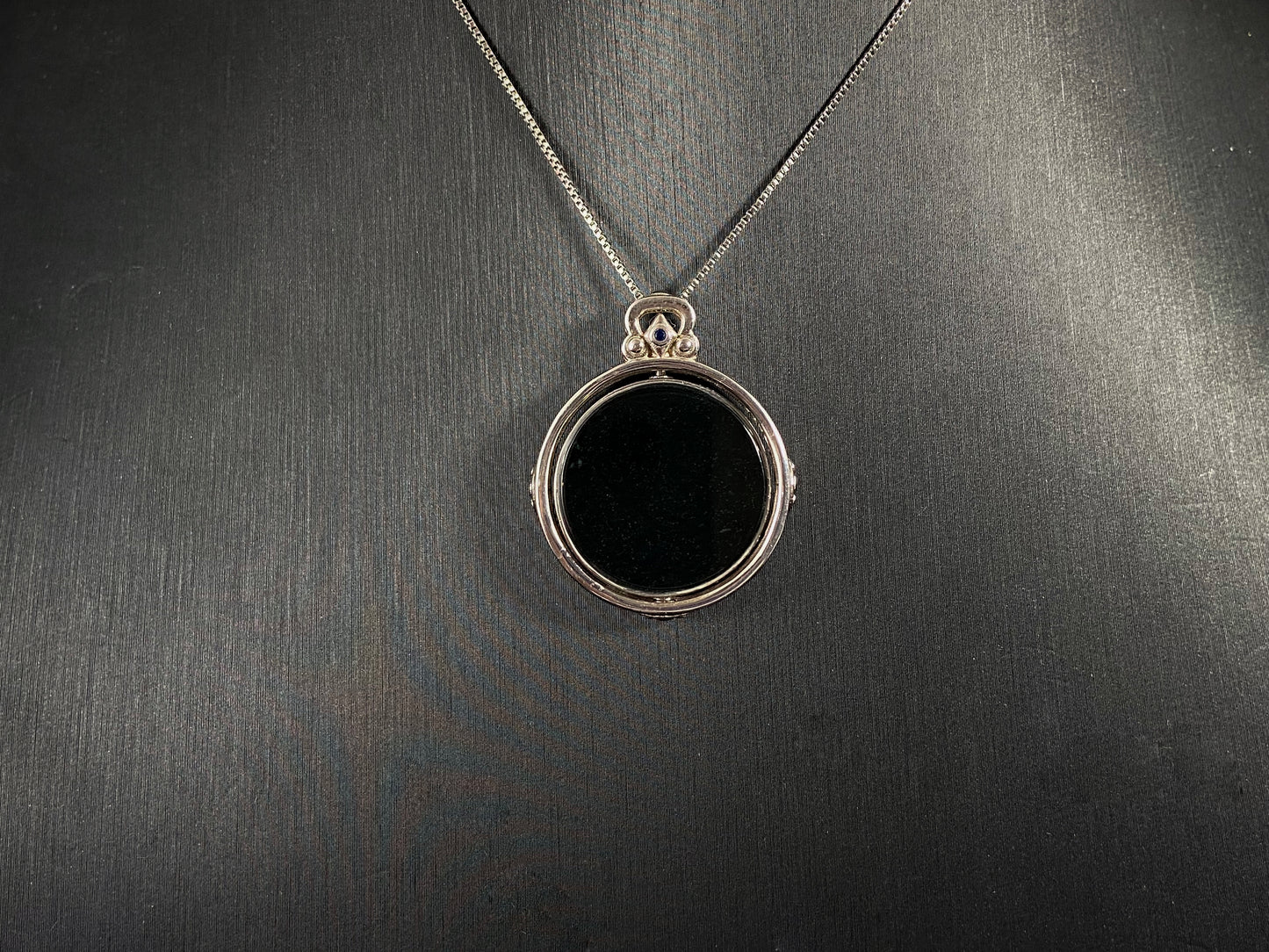Silver necklace with a round pendant on a dark gray background