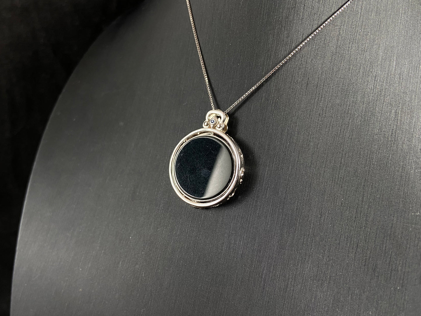 Silver necklace with a round pendant on a dark gray background