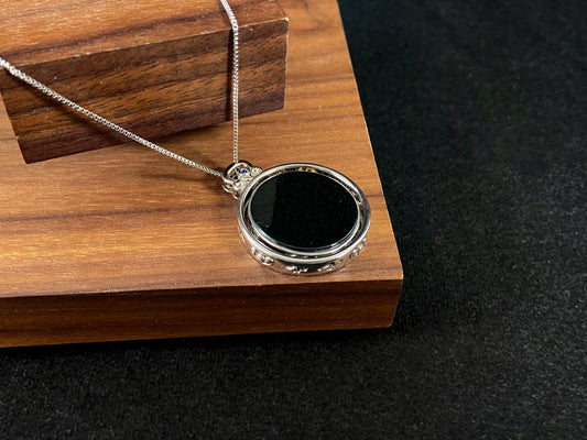 Silver necklace with a black pendant on a wooden stand against a dark background