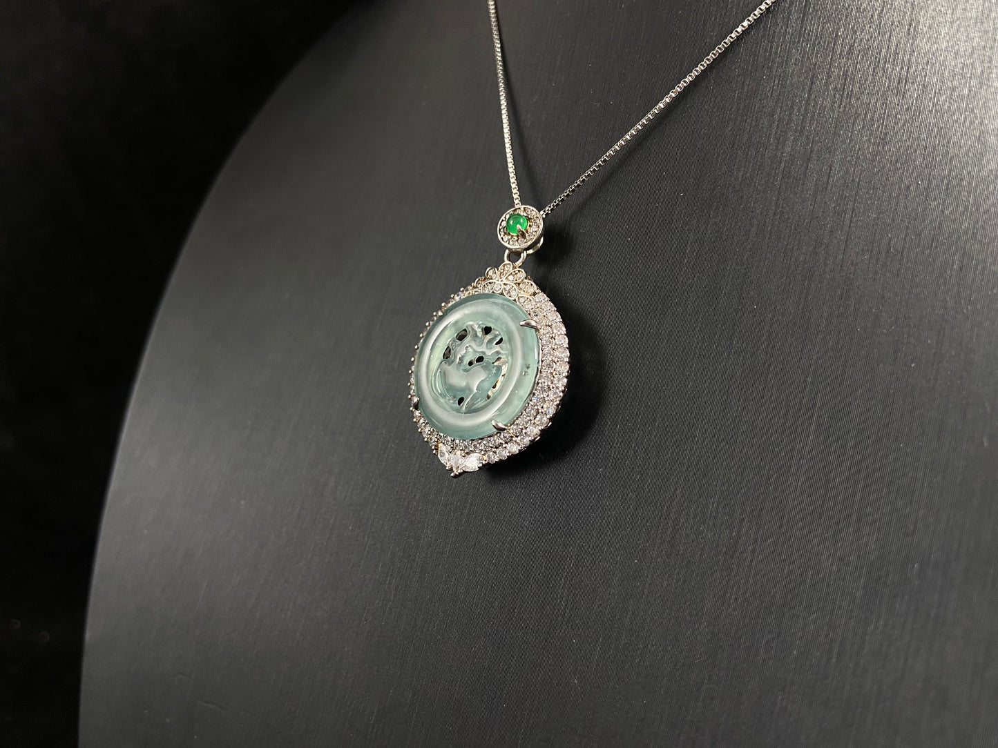 A circular pendant features a light green jade deer enclosed within a jade ring, all framed in 925 silver.