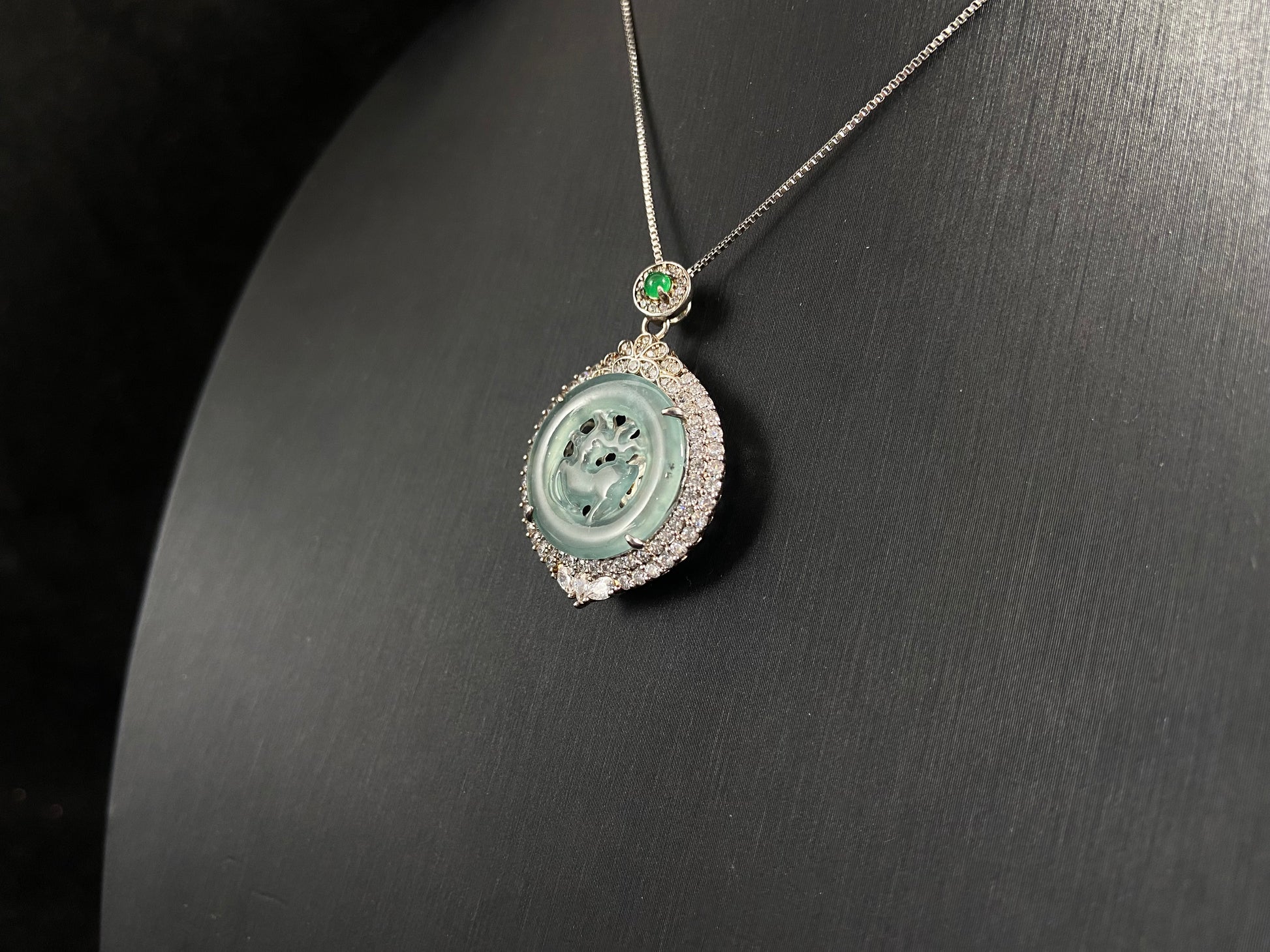 A circular pendant features a light green jade deer enclosed within a jade ring, all framed in 925 silver.