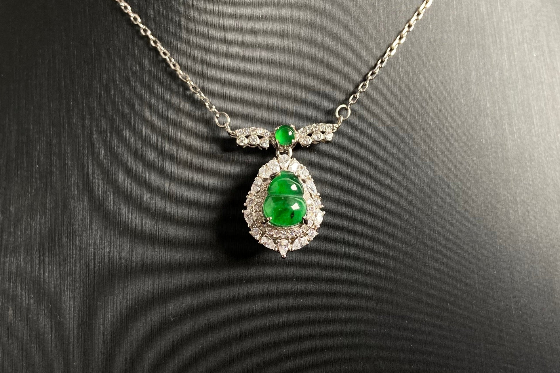 An imperial green jade gourd pendant adorned with a green bead atop, elegantly framed in 925 silver.