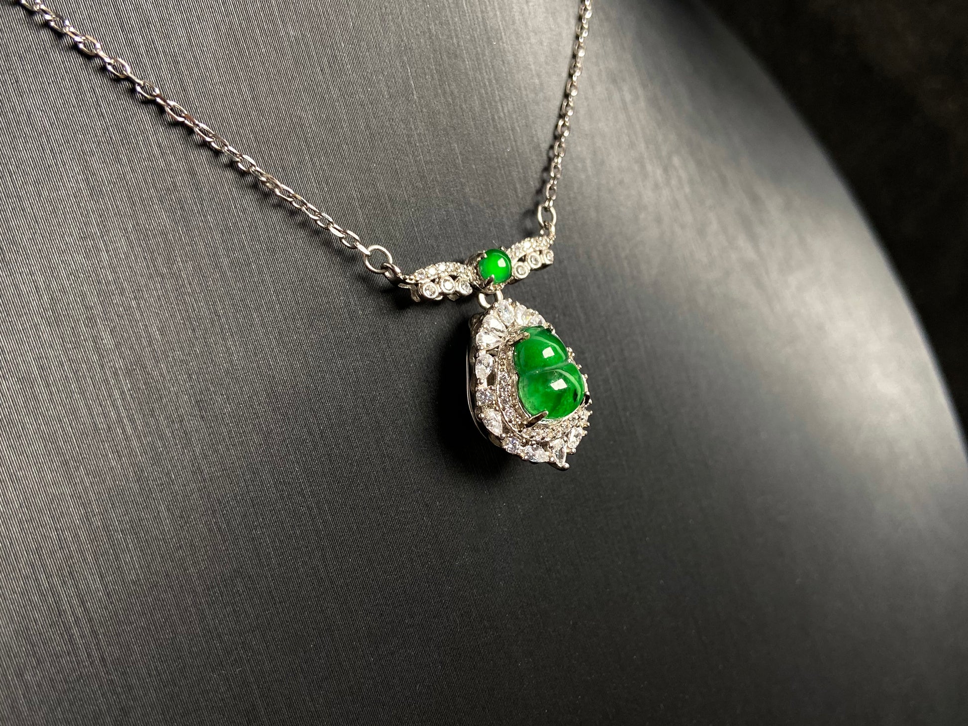 A silver framed green jadeite Gourd pendant, topped with a bead and backed by a gold money bag symbolizing wealth and power.