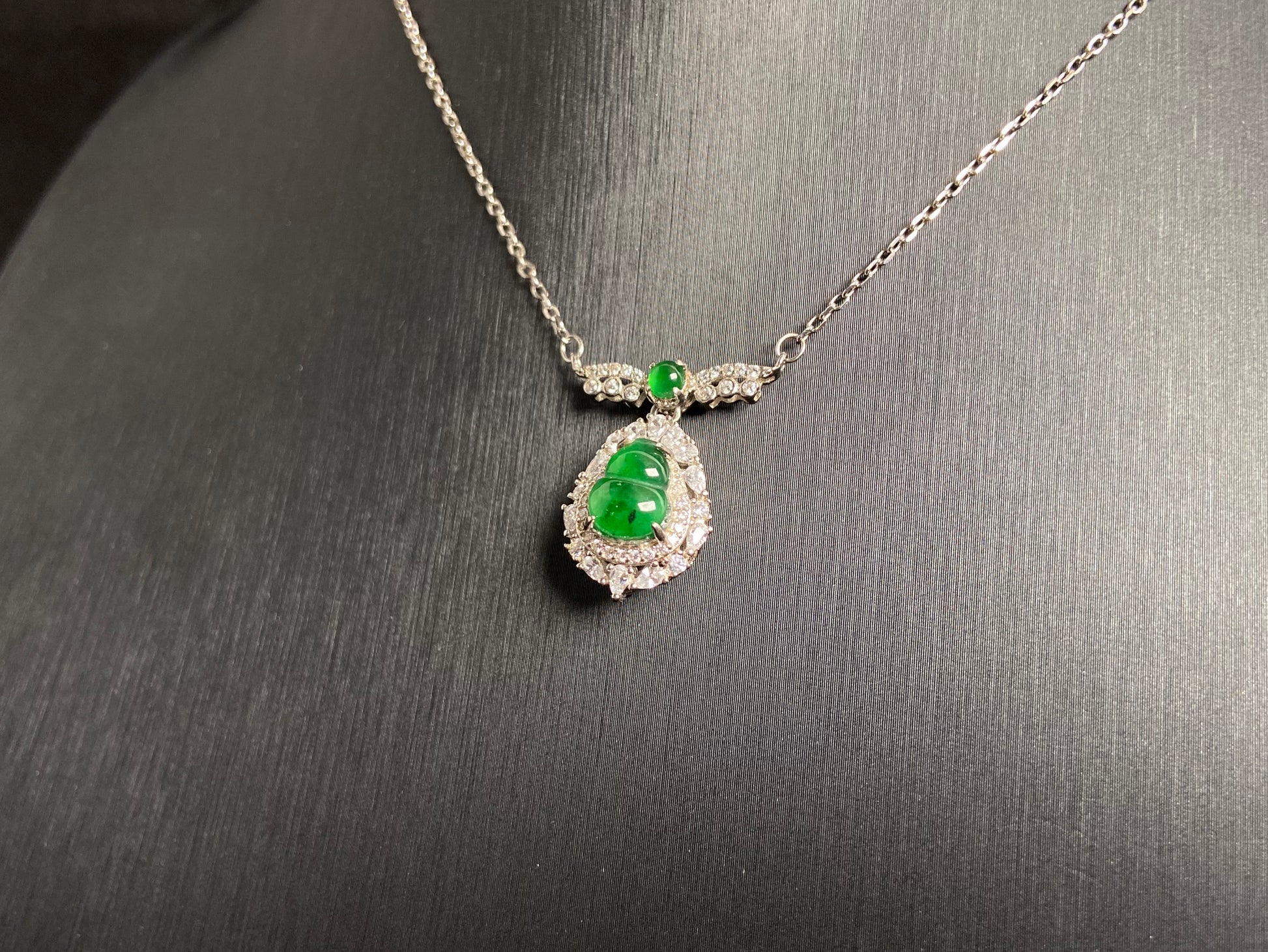 A silver framed green jadeite Gourd pendant, topped with a bead and backed by a gold money bag symbolizing wealth and power.