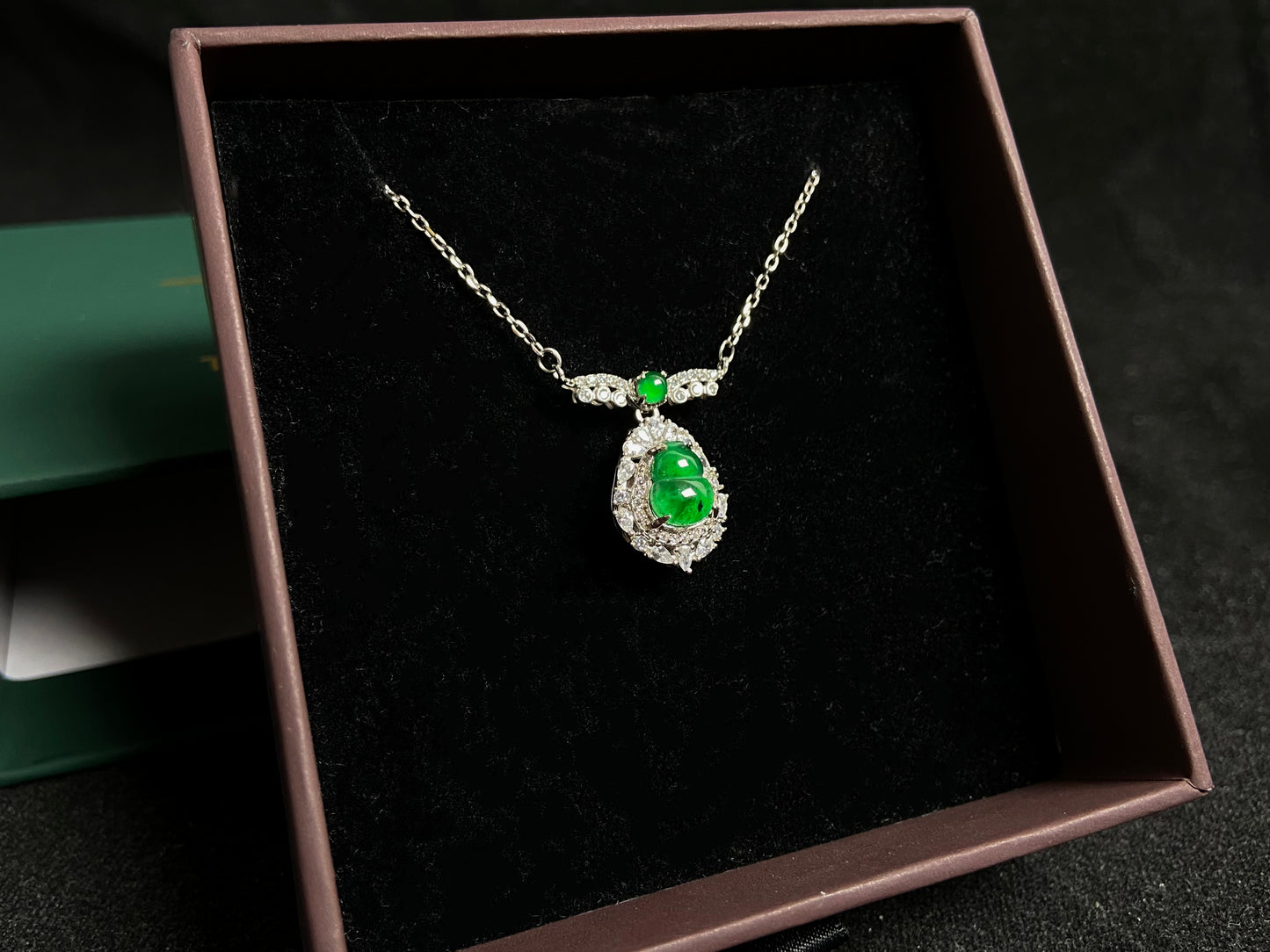 A silver framed green jadeite Gourd pendant, topped with a bead and backed by a gold money bag symbolizing wealth and power.