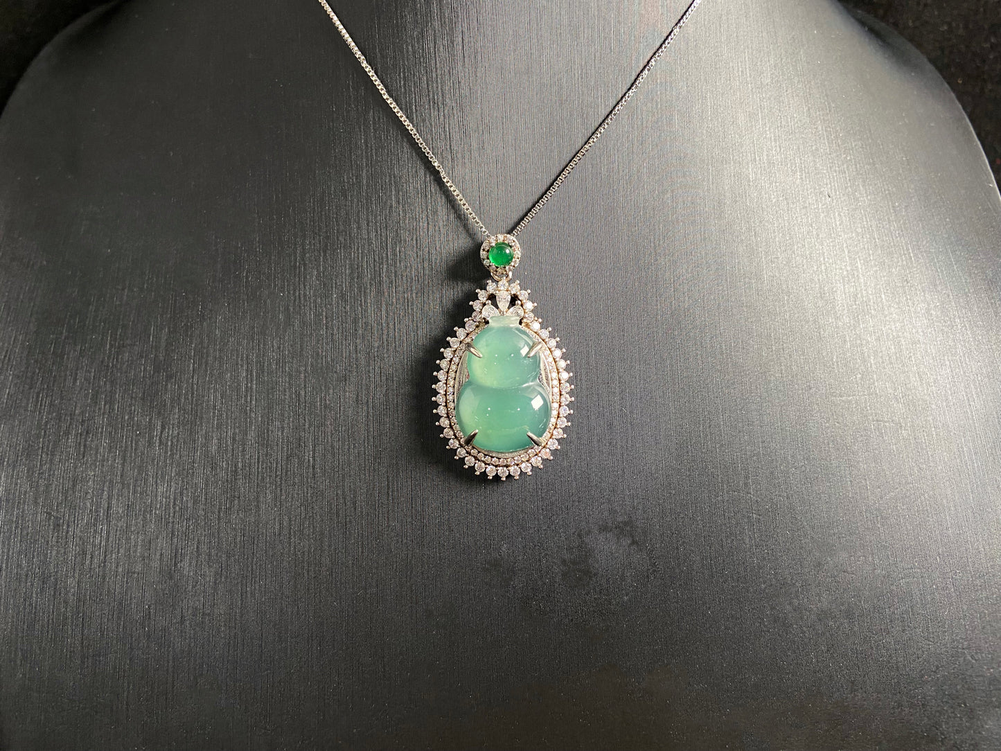 This jade pendant features a serene aqua green Hulu(gourd) accented with a regal imperial green jade bead, both elegantly set in 925 silver.