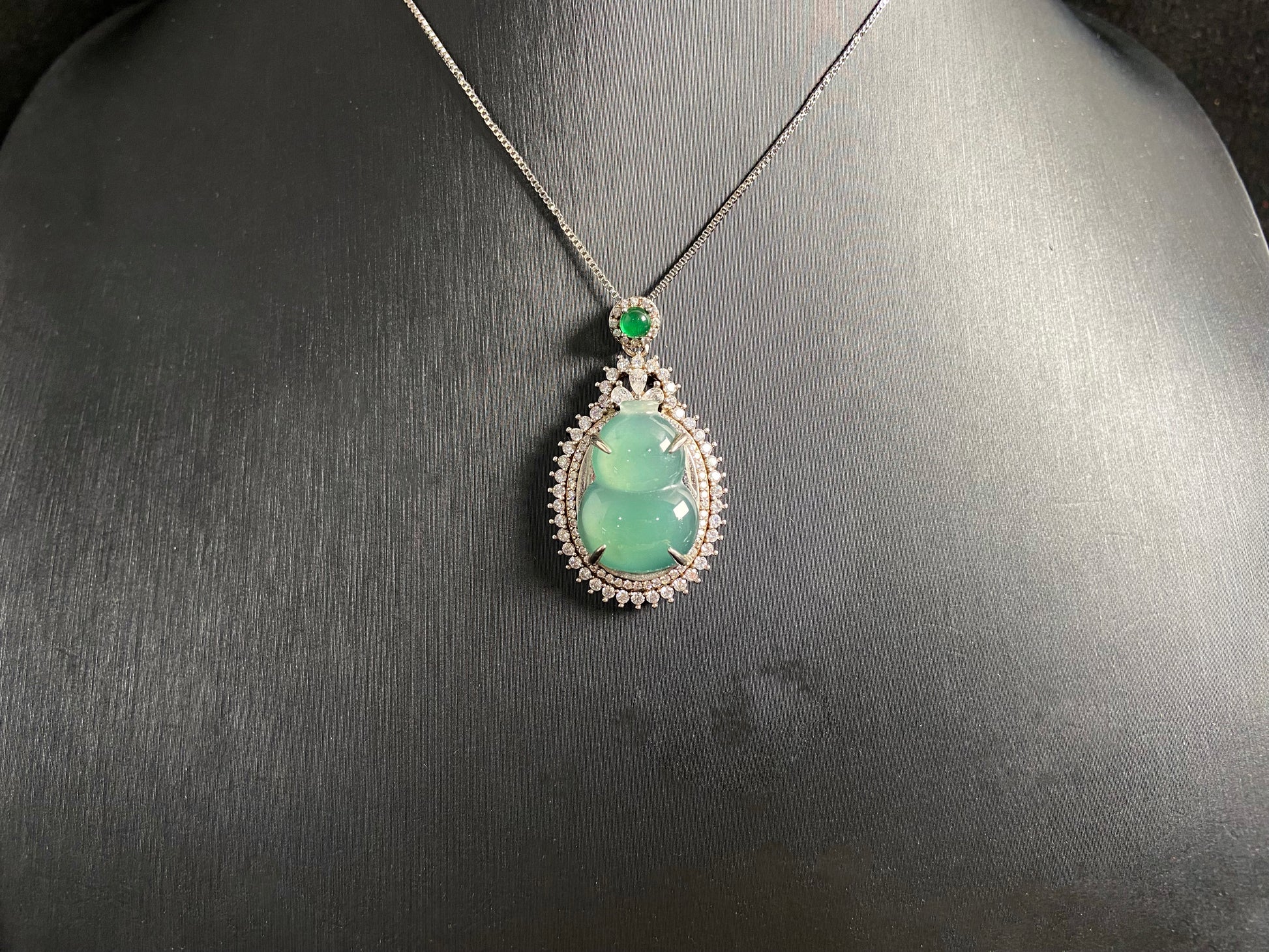 This jade pendant features a serene aqua green Hulu(gourd) accented with a regal imperial green jade bead, both elegantly set in 925 silver.
