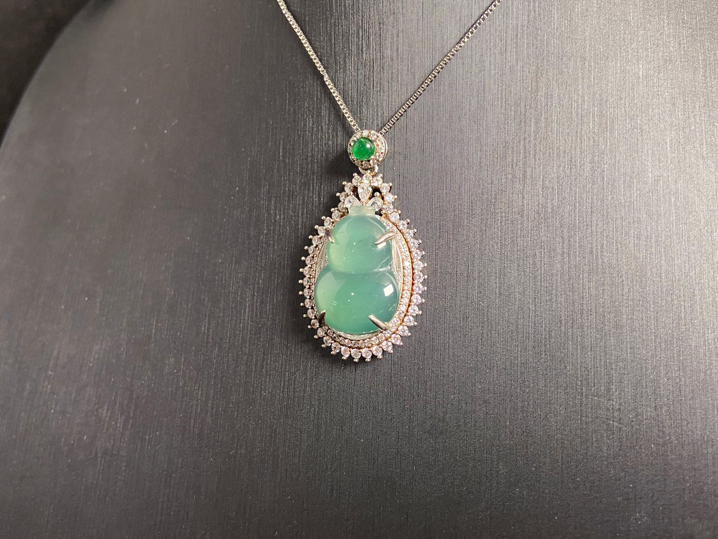This jade pendant features a serene aqua green Hulu(gourd) accented with a regal imperial green jade bead, both elegantly set in 925 silver.