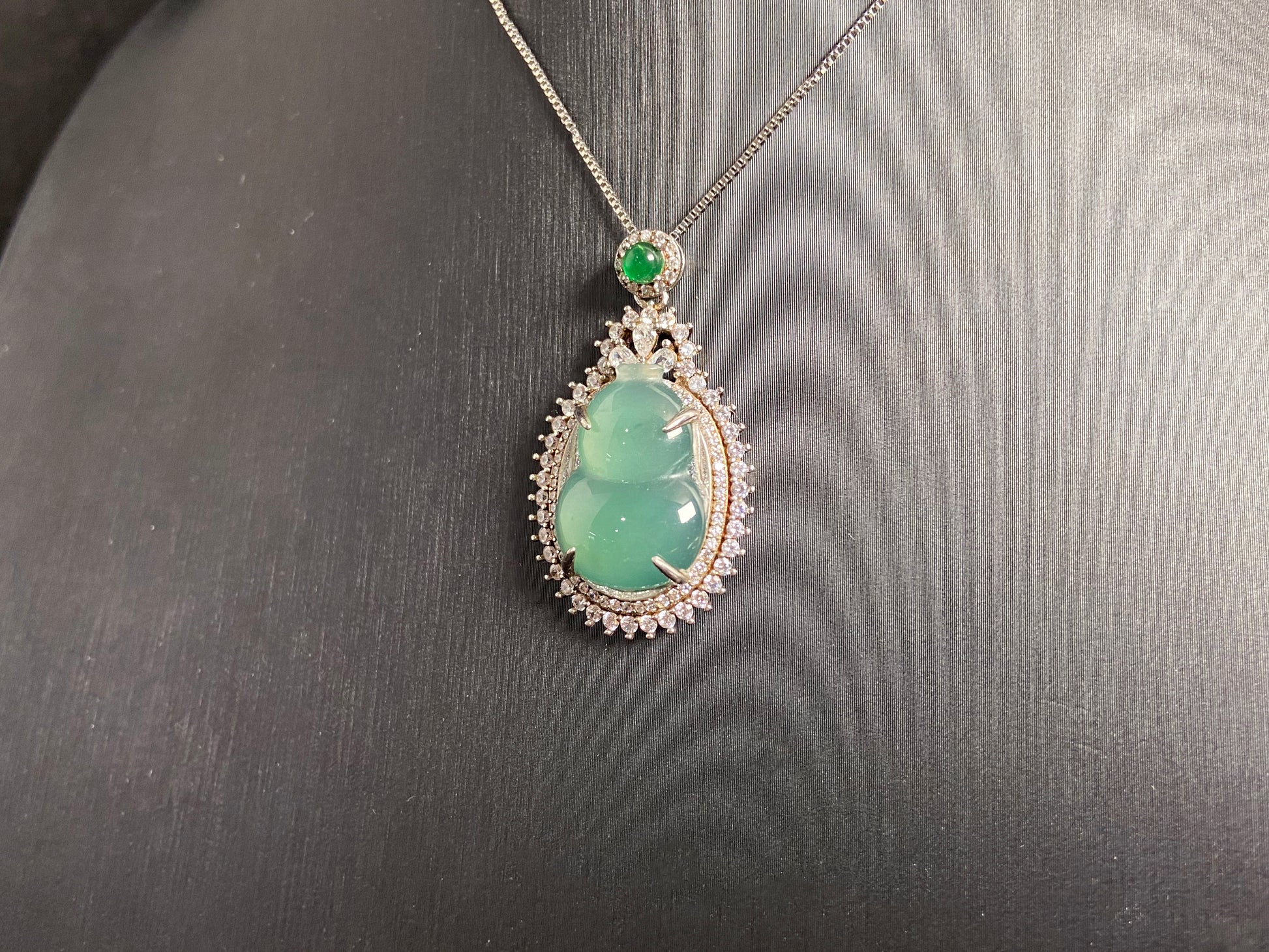 This jade pendant features a serene aqua green Hulu(gourd) accented with a regal imperial green jade bead, both elegantly set in 925 silver.