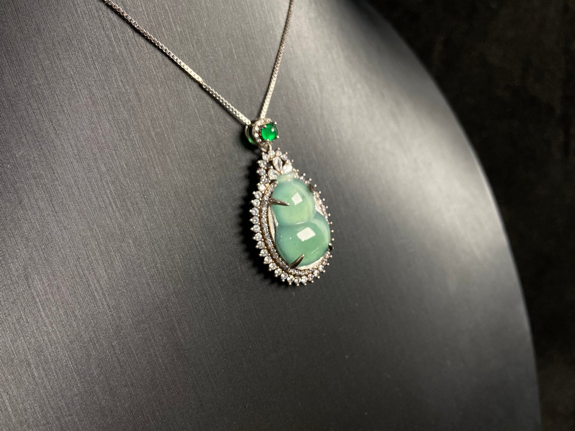 This jade pendant features a serene aqua green Hulu(gourd) accented with a regal imperial green jade bead, both elegantly set in 925 silver.