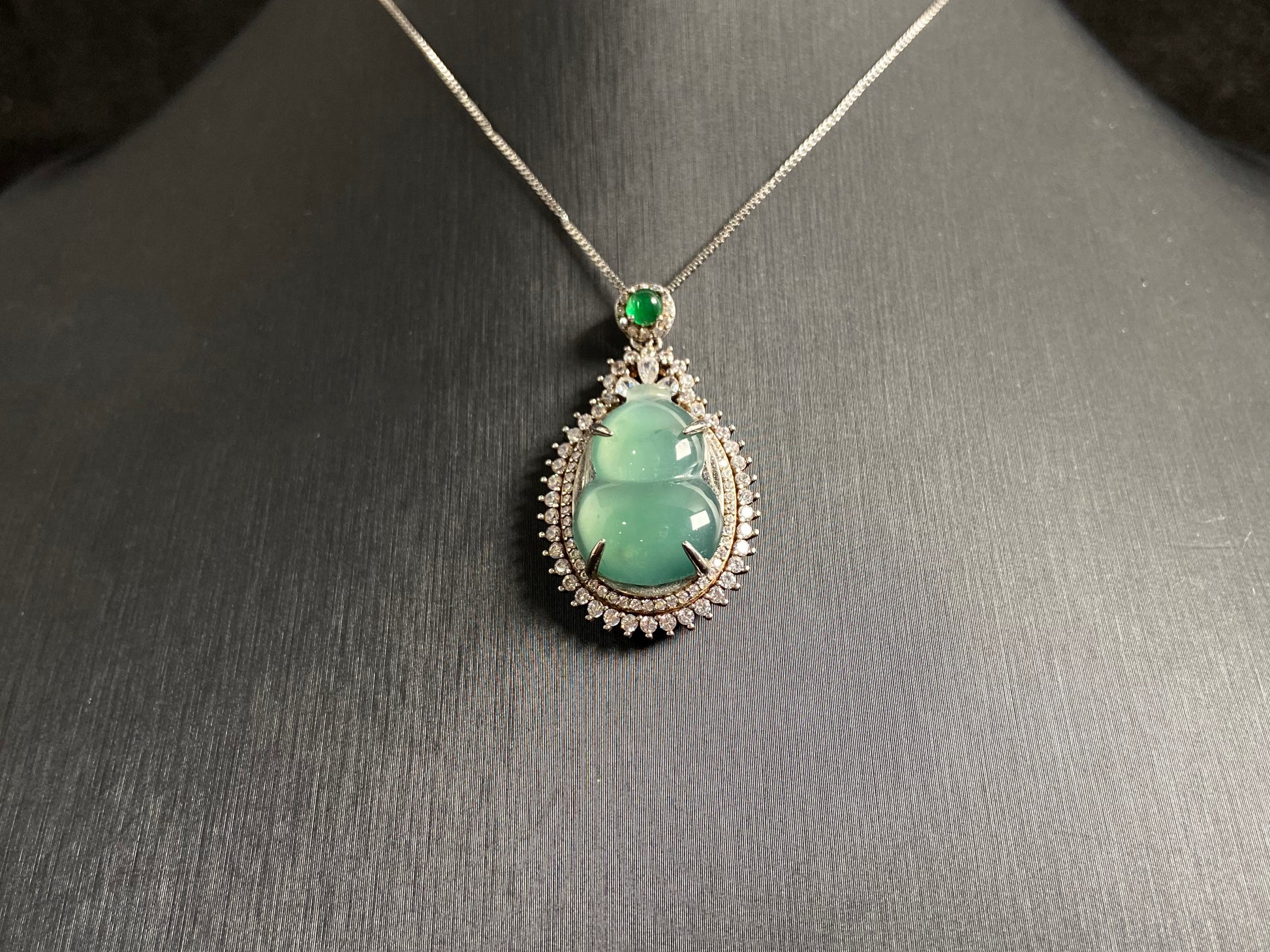 This jade pendant features a serene aqua green Hulu(gourd) accented with a regal imperial green jade bead, both elegantly set in 925 silver.