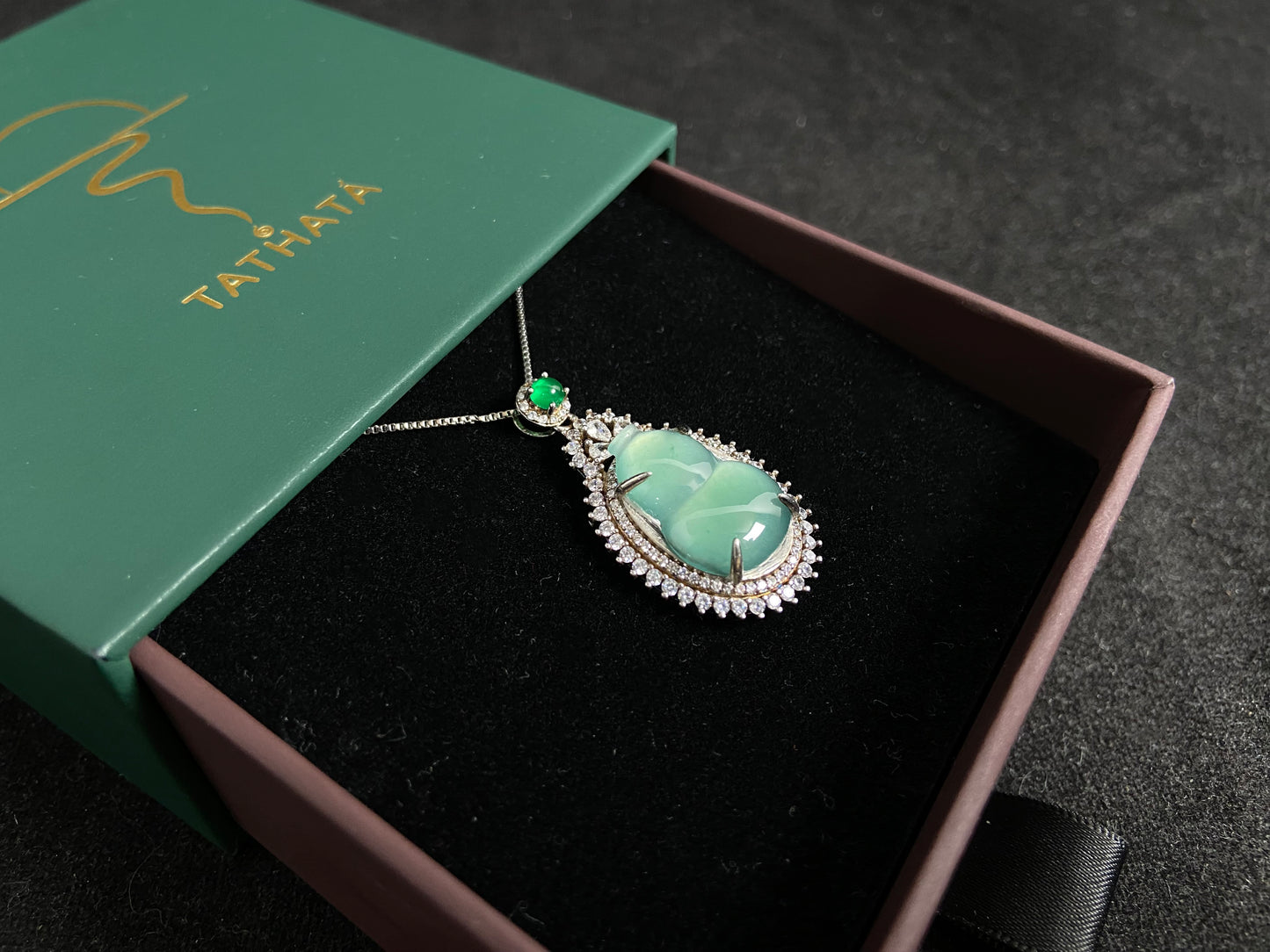 This jade pendant features a serene aqua green Hulu(gourd) accented with a regal imperial green jade bead, both elegantly set in 925 silver.