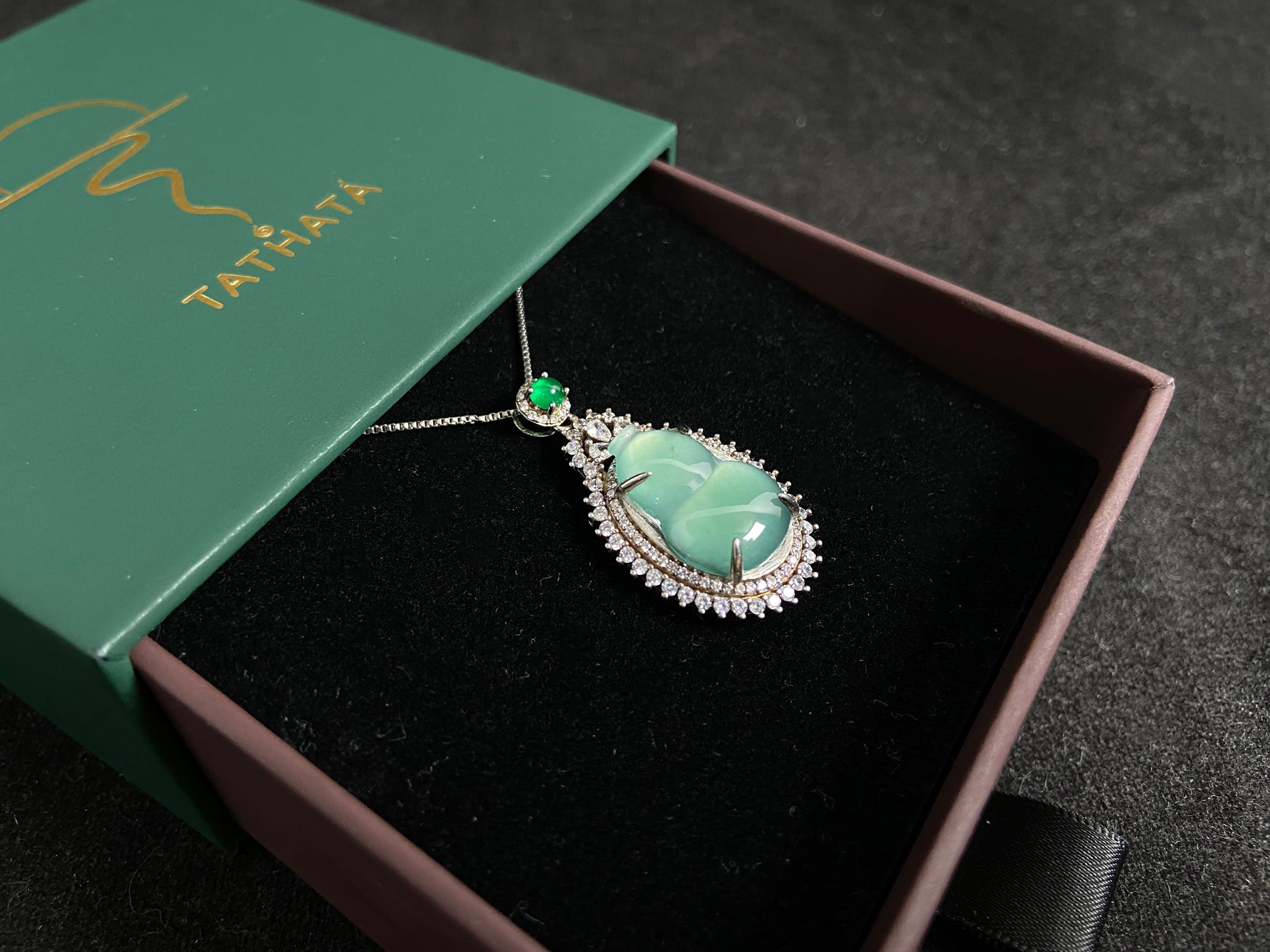 This jade pendant features a serene aqua green Hulu(gourd) accented with a regal imperial green jade bead, both elegantly set in 925 silver.