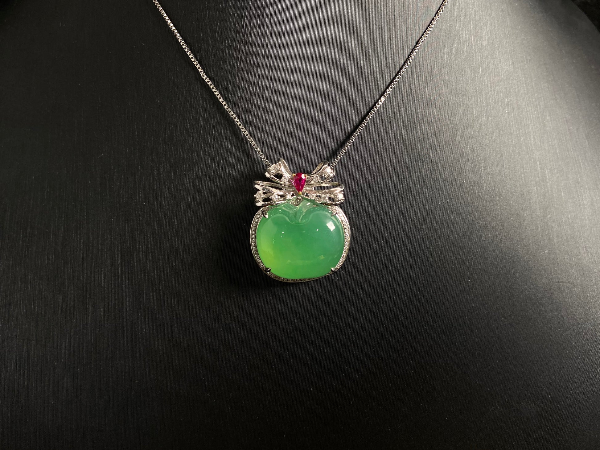 This jade pendant features an apple green jadeite apple adorned with an 18K gold bow centered with a rose gold accent.