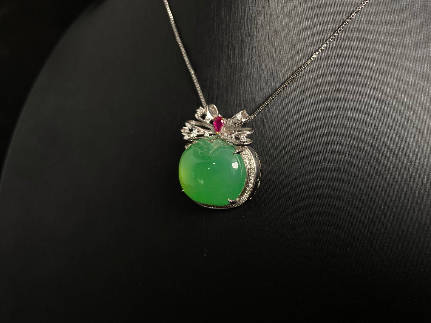 This jade pendant features an apple green jadeite apple adorned with an 18K gold bow centered with a rose gold accent.