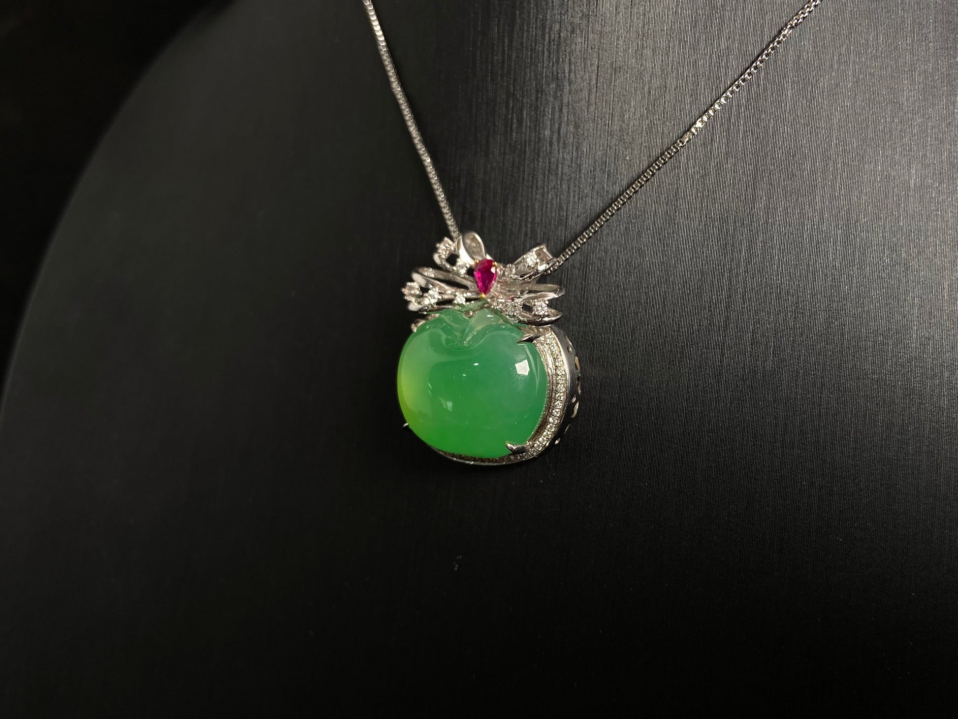 This jade pendant features an apple green jadeite apple adorned with an 18K gold bow centered with a rose gold accent.