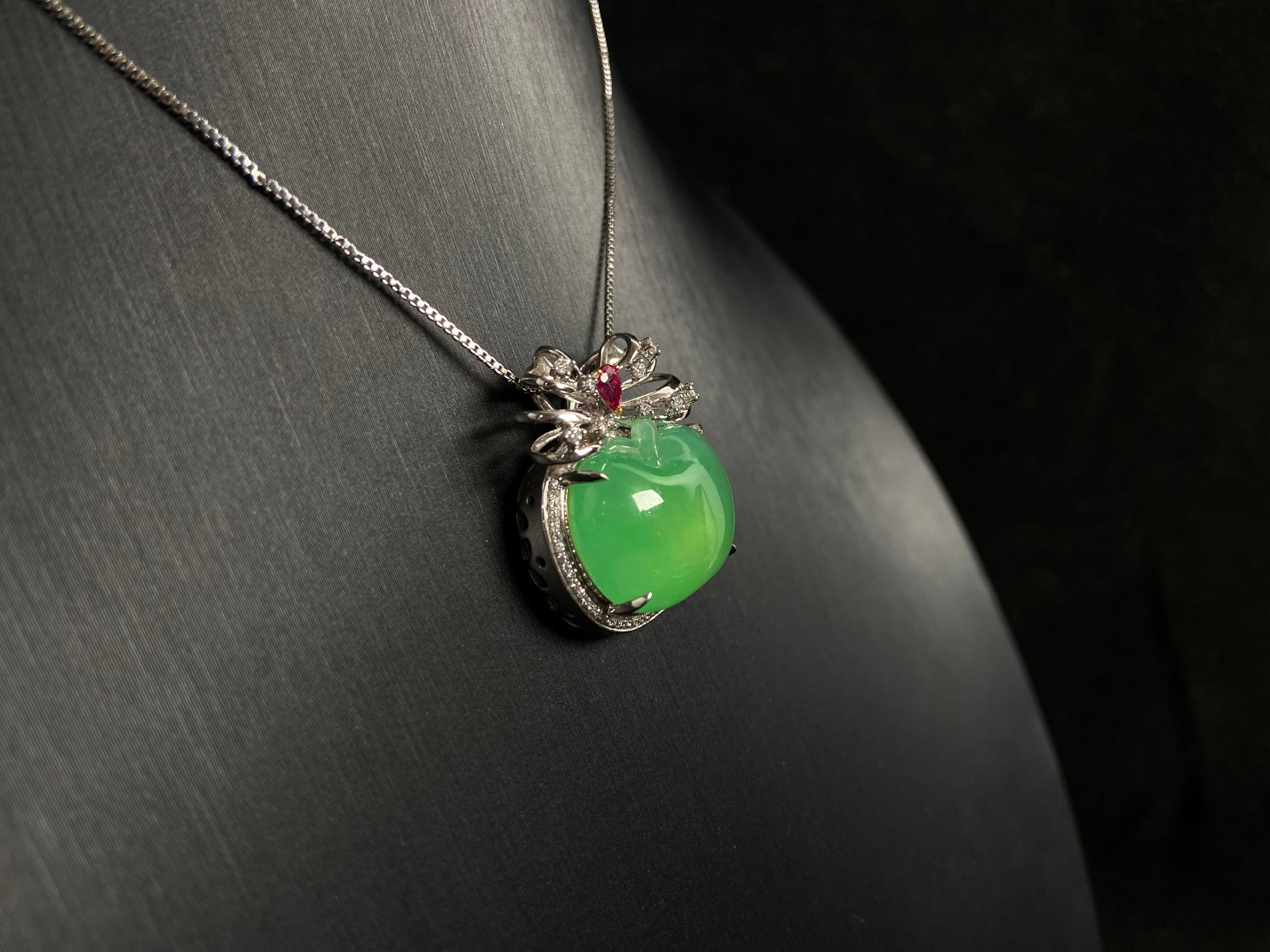 This jade pendant features an apple green jadeite apple adorned with an 18K gold bow centered with a rose gold accent.