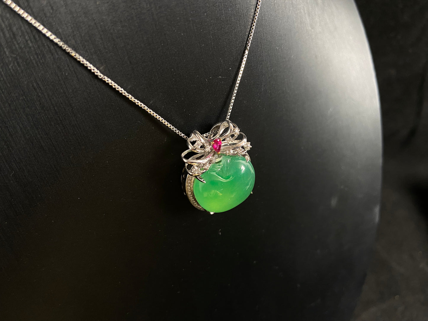 This jade pendant features an apple green jadeite apple adorned with an 18K gold bow centered with a rose gold accent.
