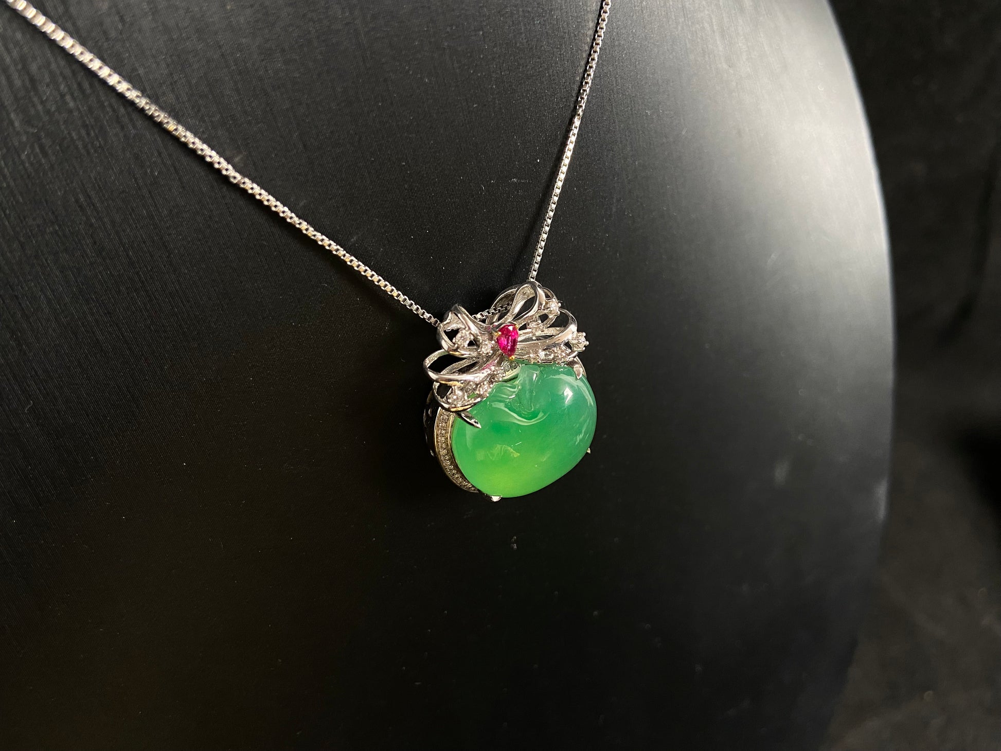 This jade pendant features an apple green jadeite apple adorned with an 18K gold bow centered with a rose gold accent.