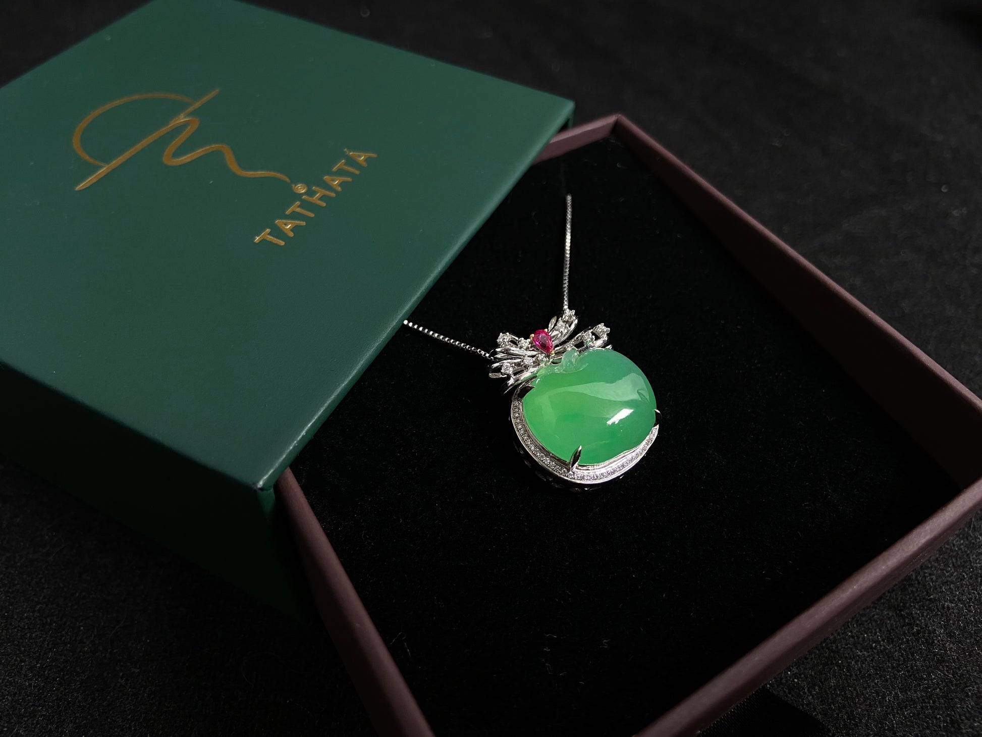 This jade pendant features an apple green jadeite apple adorned with an 18K gold bow centered with a rose gold accent.