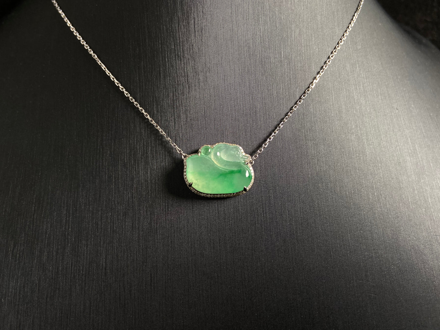 This jadeite pendant features a light green, translucent swan with deep green inclusions, elegantly set in 18K gold.