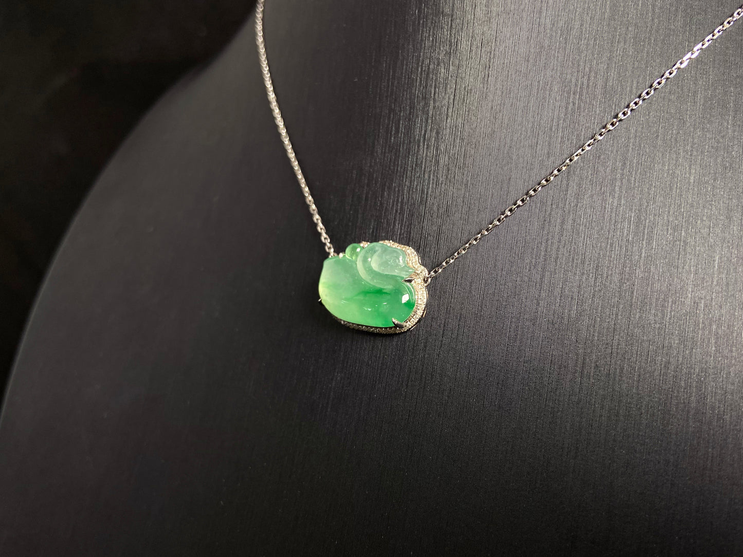 This jadeite pendant features a light green, translucent swan with deep green inclusions, elegantly set in 18K gold.
