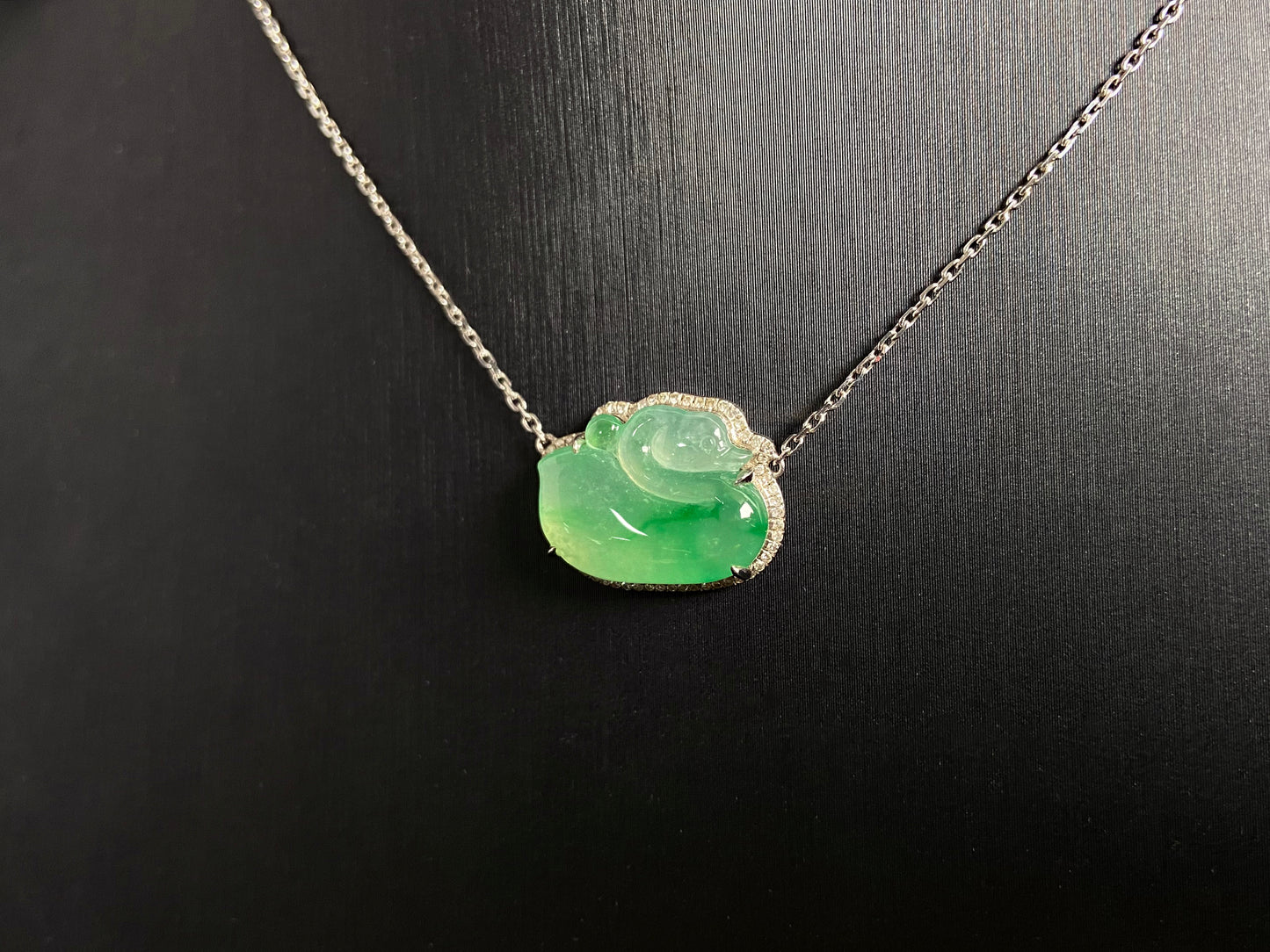 This jadeite pendant features a light green, translucent swan with deep green inclusions, elegantly set in 18K gold.