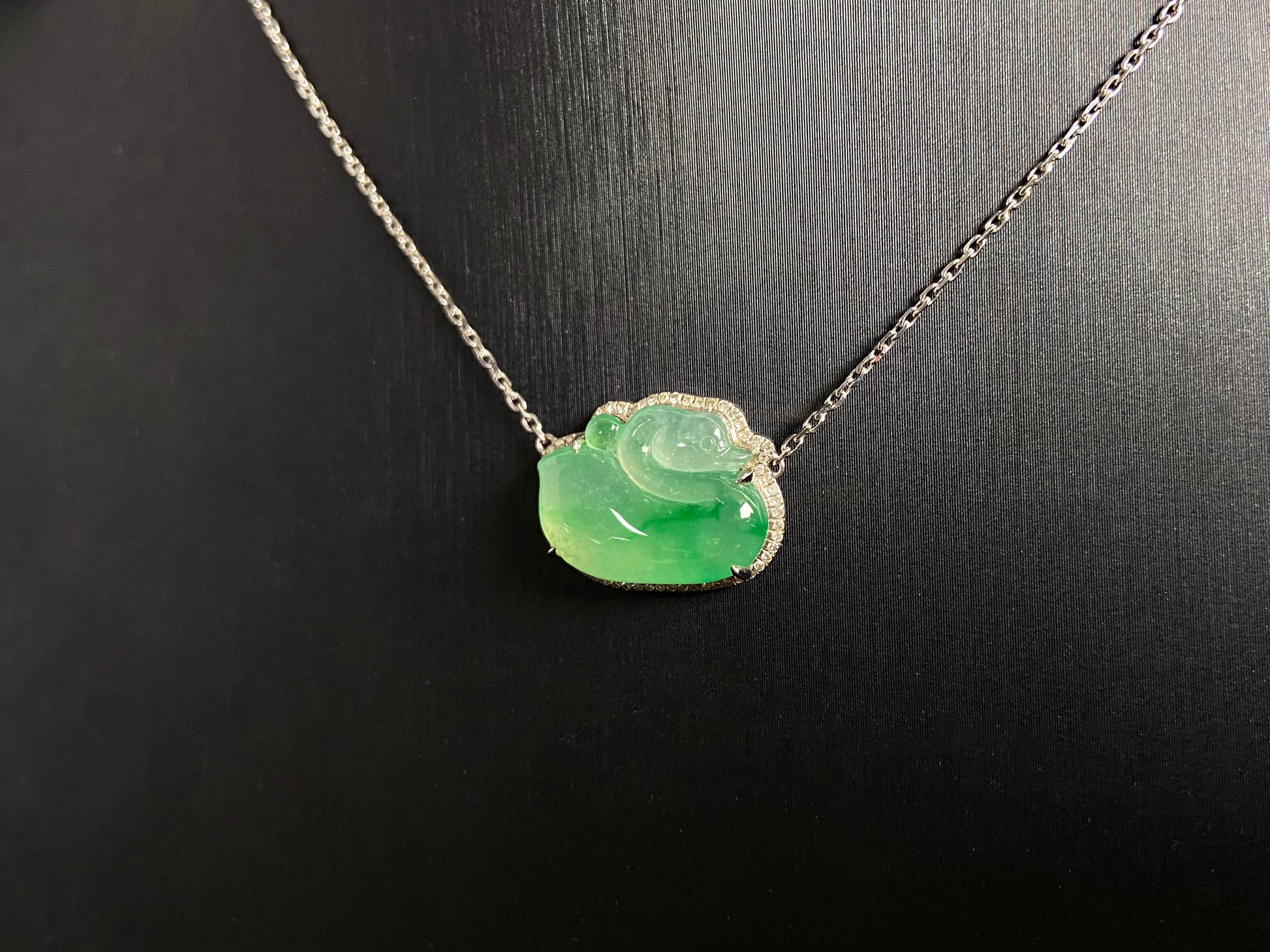This jadeite pendant features a light green, translucent swan with deep green inclusions, elegantly set in 18K gold.