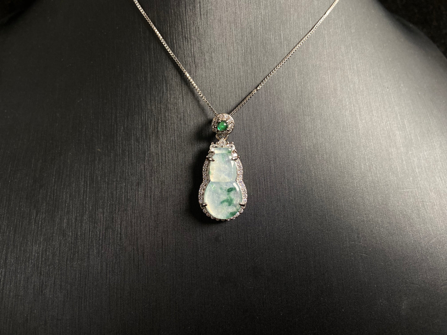 This jade pendant features a translucent white Hulu with natural dark green veining, crowned with an imperial green jade bead and set in 925 silver.