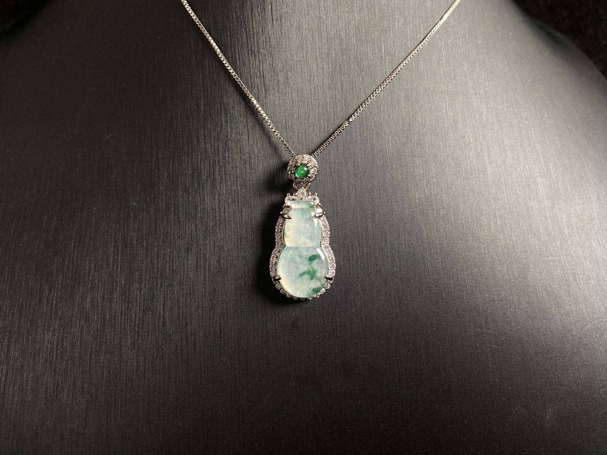 This jade pendant features a translucent white Hulu with natural dark green veining, crowned with an imperial green jade bead and set in 925 silver.