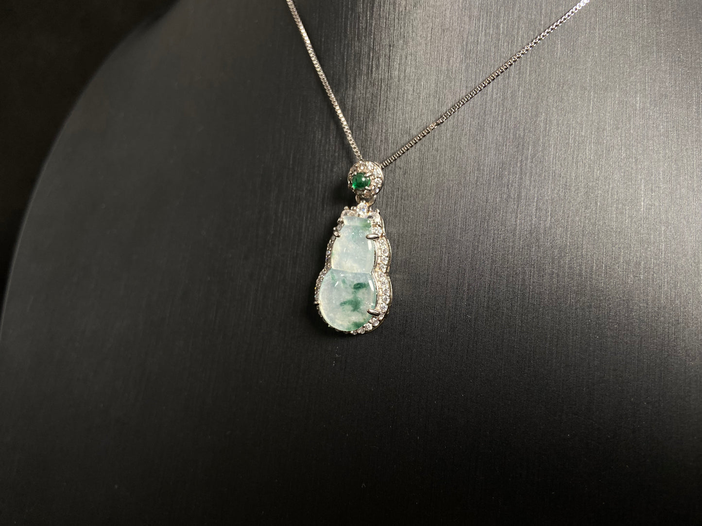 This jade pendant features a translucent white Hulu with natural dark green veining, crowned with an imperial green jade bead and set in 925 silver.