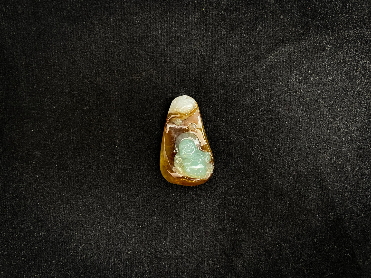 This jade pendant features a brown jade base with white accents, cradling a light green reclining Maitreya Buddha in its design.