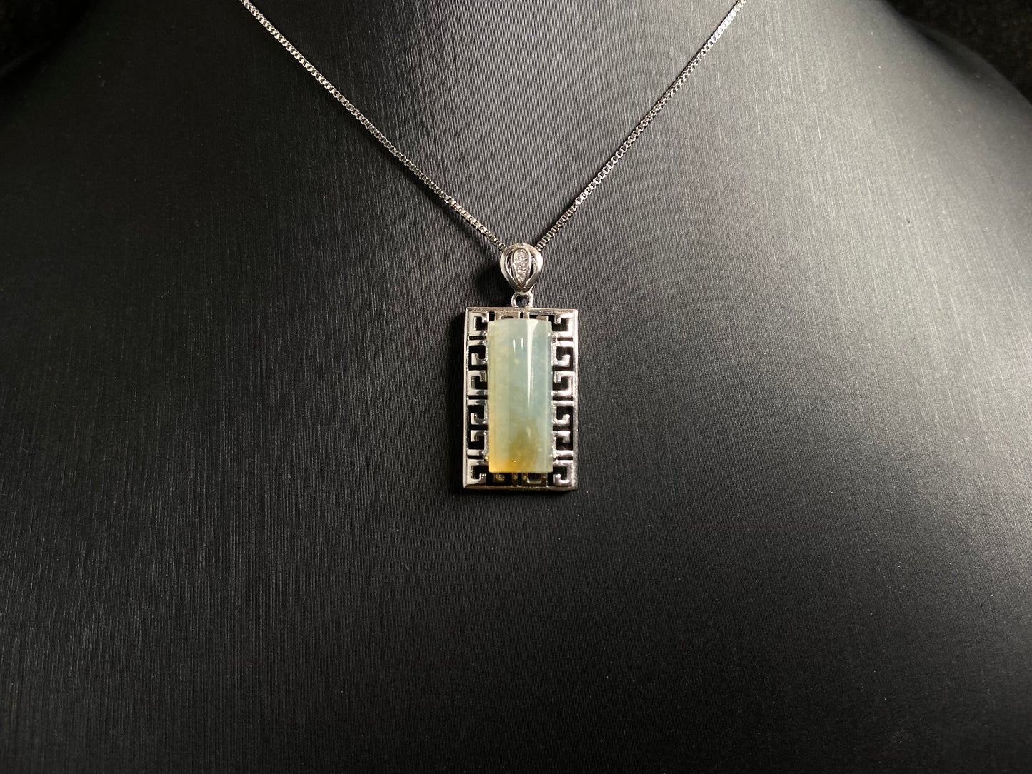 This unique jade pendant features a semi cylindrical column design with a subtle yellow accent floating at its base.