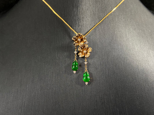 This elegant pendant showcases two emerald green jade gourds suspended from delicately crafted 18k gold flowers.