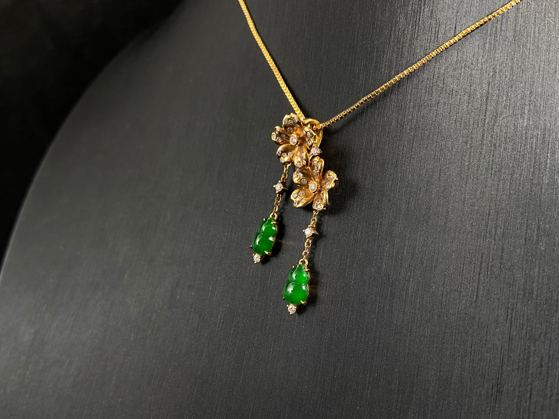 This elegant pendant showcases two emerald green jade gourds suspended from delicately crafted 18k gold flowers.
