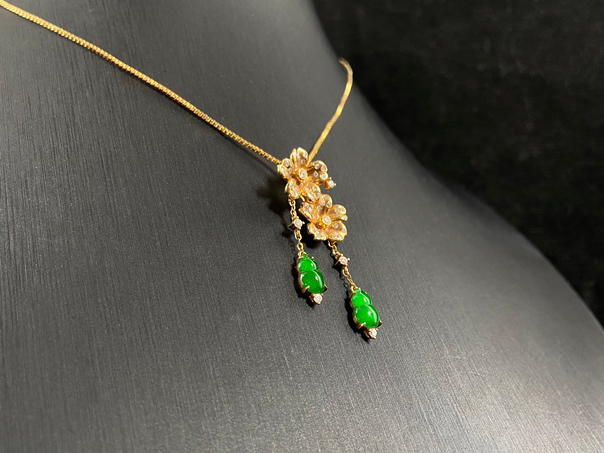 This elegant pendant showcases two emerald green jade gourds suspended from delicately crafted 18k gold flowers.