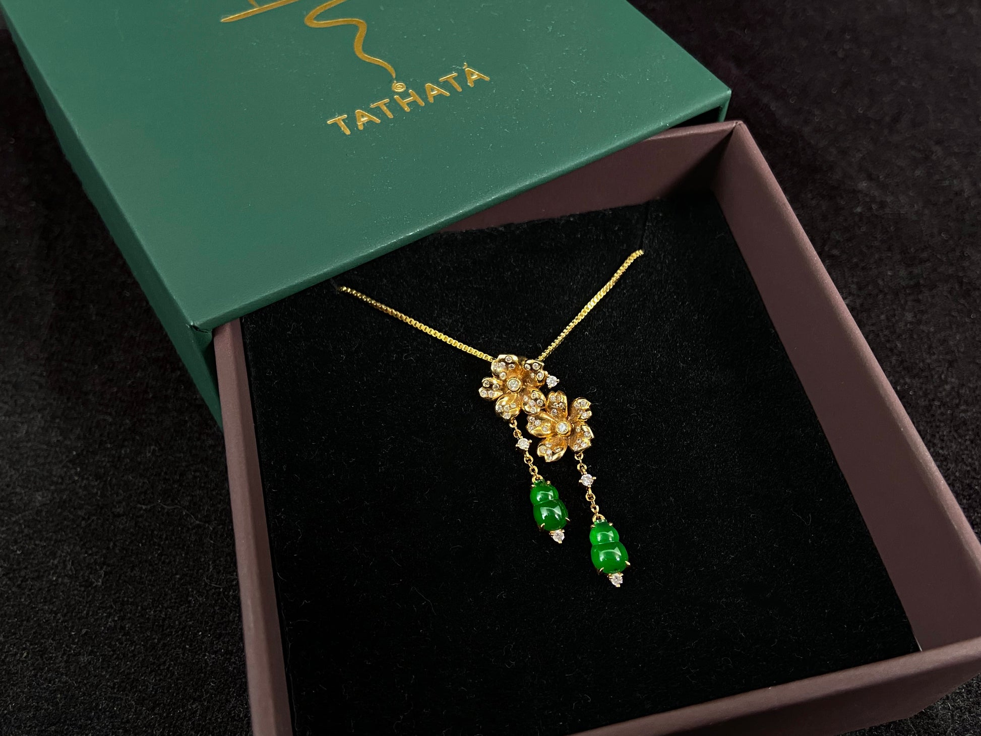 This elegant pendant showcases two emerald green jade gourds suspended from delicately crafted 18k gold flowers.