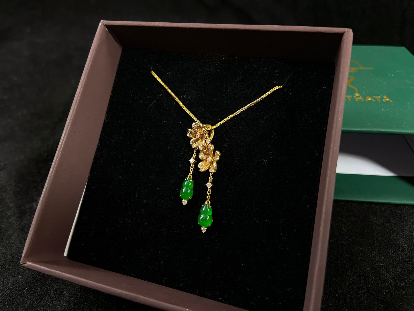 This elegant pendant showcases two emerald green jade gourds suspended from delicately crafted 18k gold flowers.
