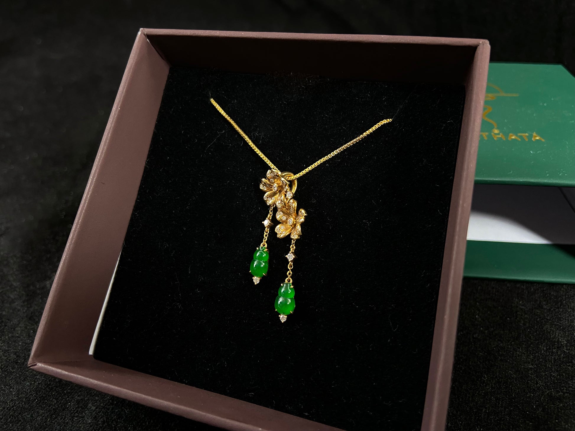 This elegant pendant showcases two emerald green jade gourds suspended from delicately crafted 18k gold flowers.