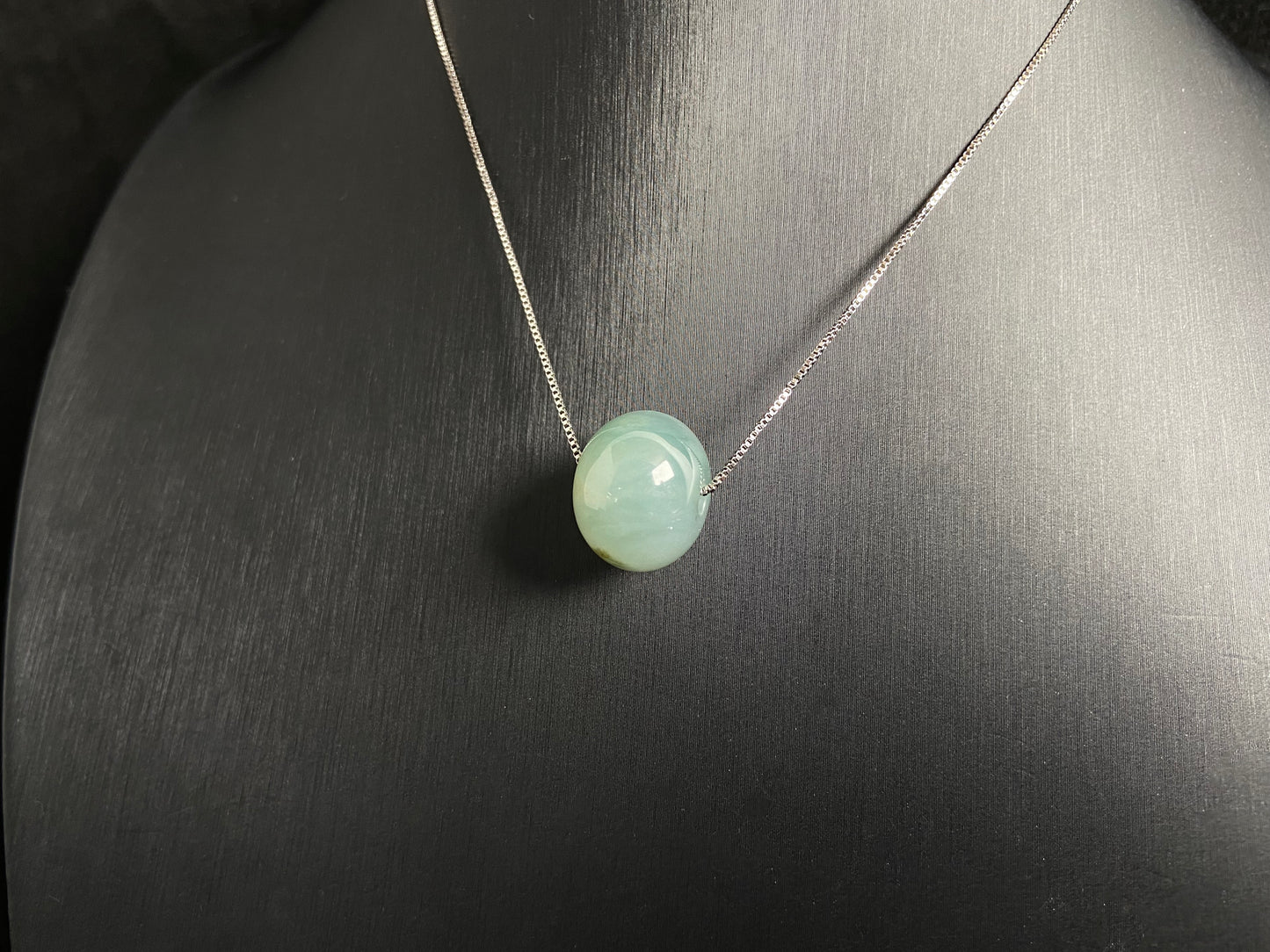 A pale green jade bead with a natural dark green accent.