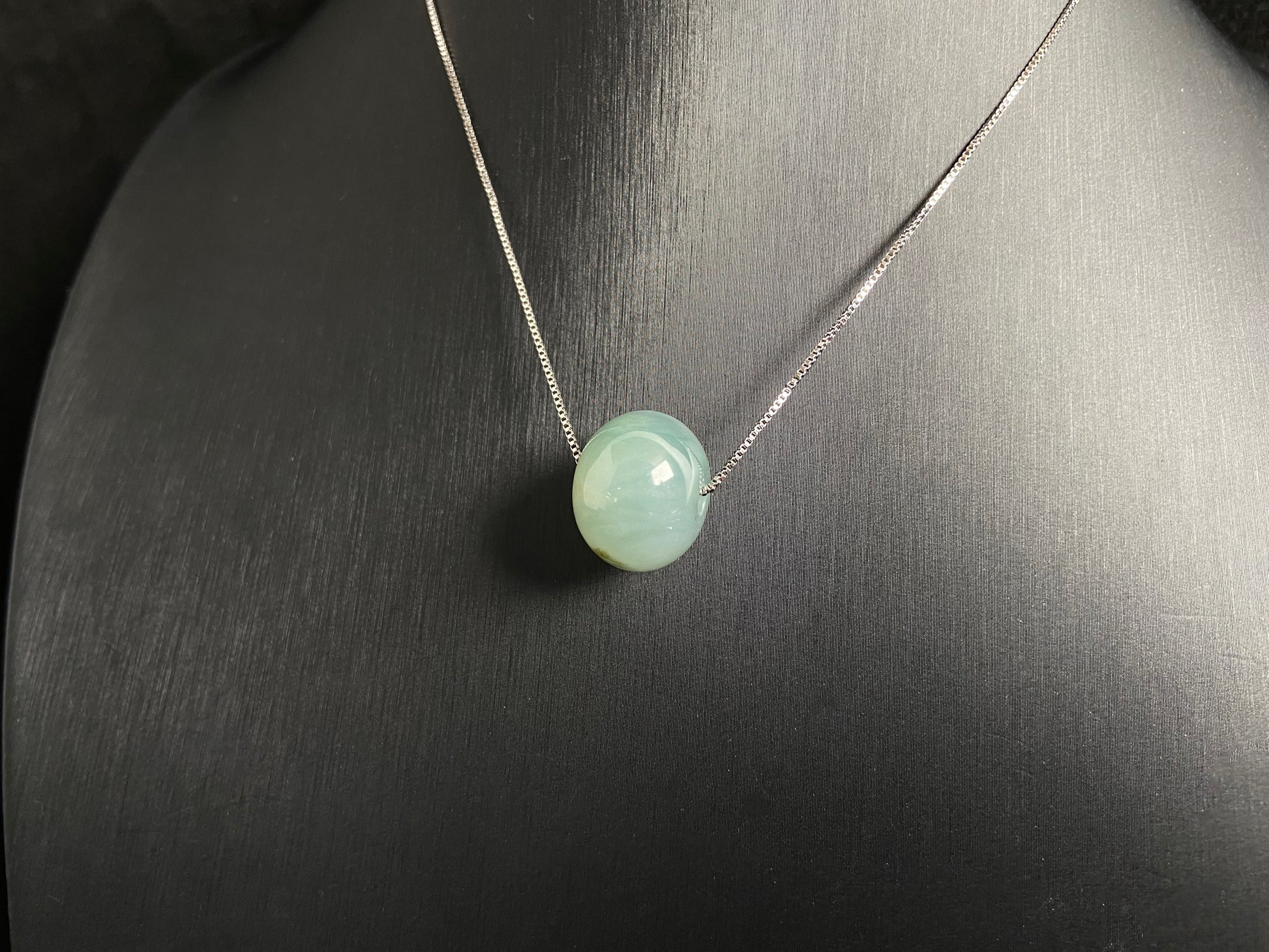 A pale green jade bead with a natural dark green accent.