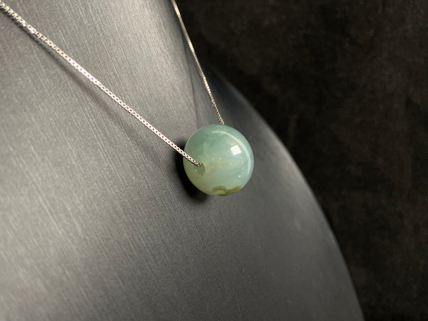 A pale green jade bead with a natural dark green accent.