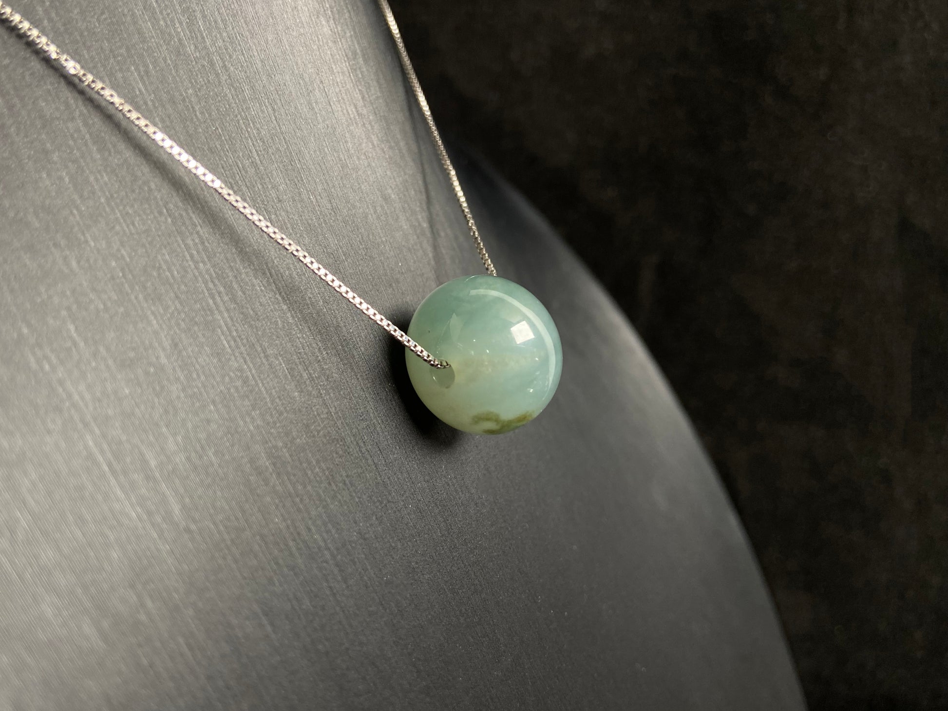 A pale green jade bead with a natural dark green accent.