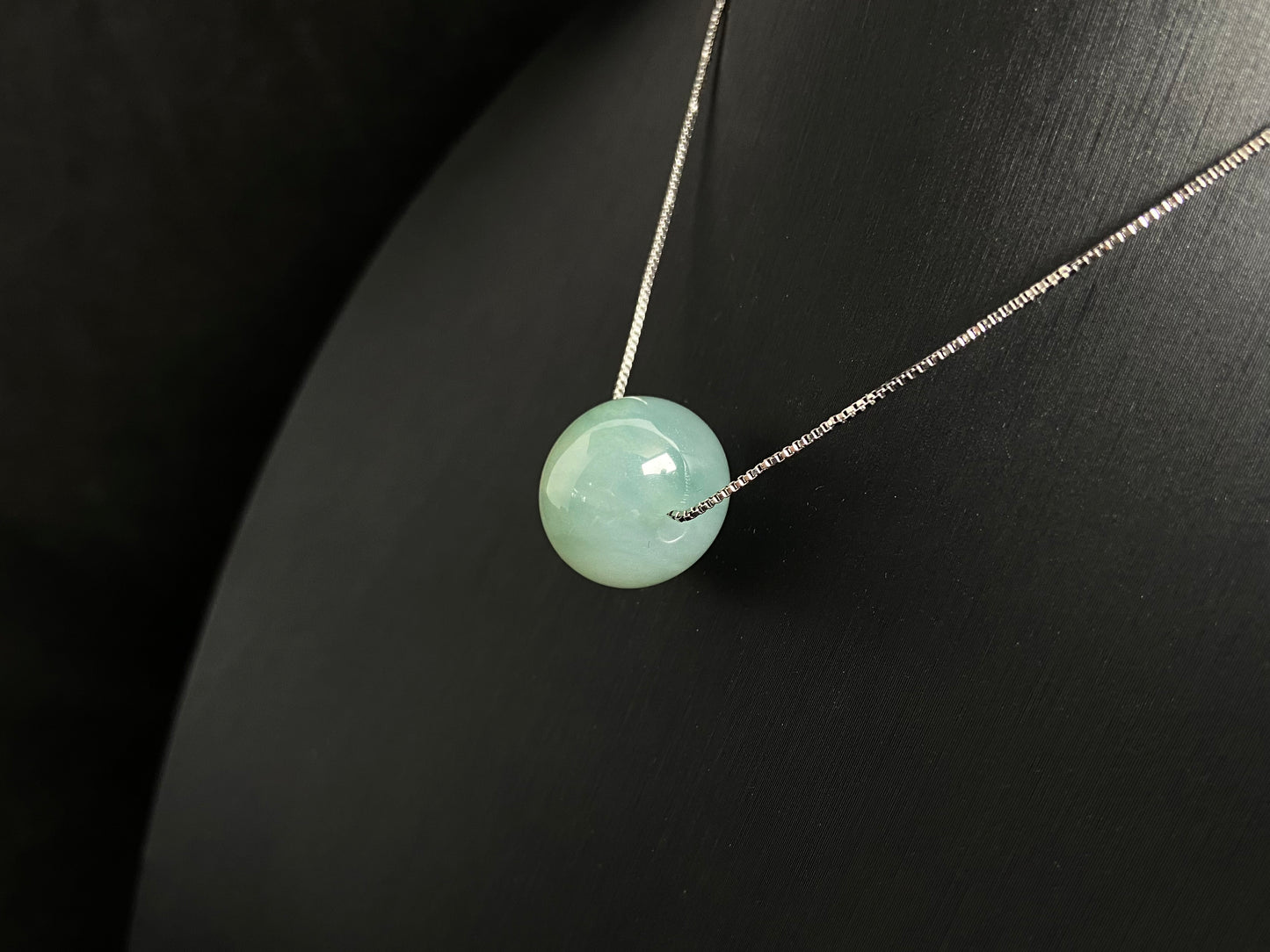A pale green jade bead with a natural dark green accent.
