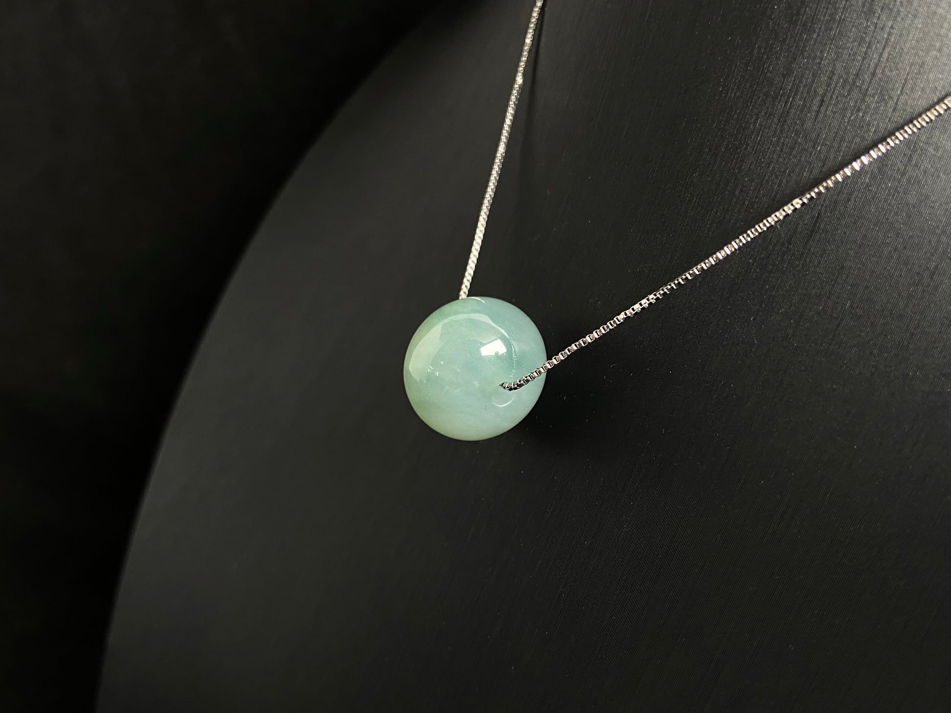 A pale green jade bead with a natural dark green accent.