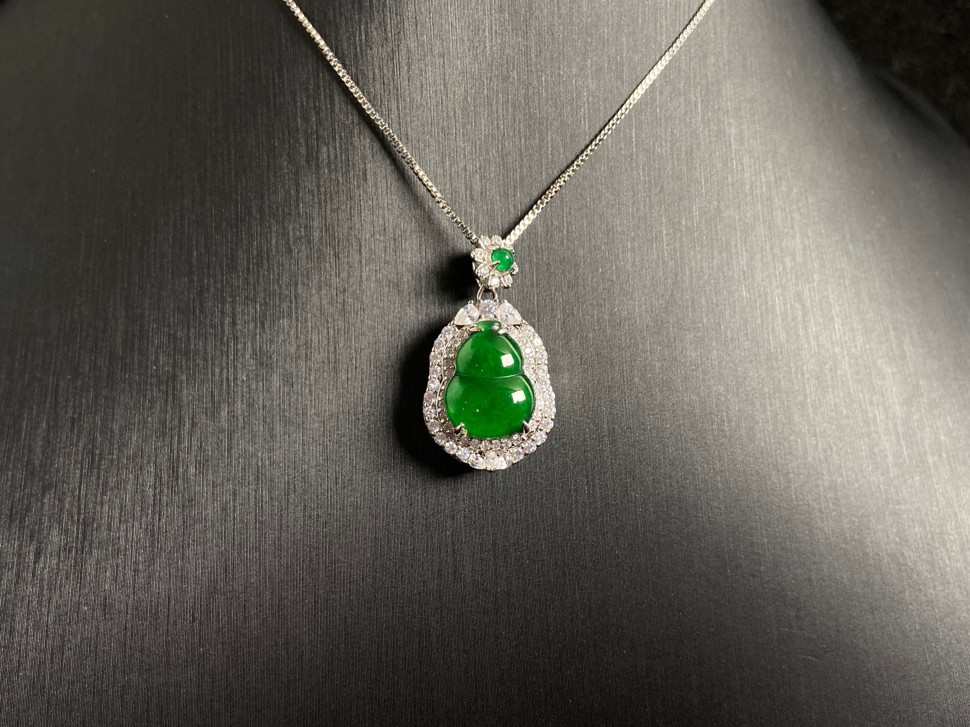 An imperial green jade gourd pendant, embraced by a diamond studded 925 silver frame.